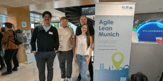Zu sehen sind vier Teammitglieder des Projektes PRAESCO neben einem Schild mit den Worten "Agile Lean Munich" Von links nach rechts sind es Ali Askari, Henrik Sellmann, Fabian Biebl Ronda Ringfort-Felner.